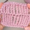 Hands holding a small swatch of pink knitted fabric, showcasing a detailed triple treble crochet stitch pattern.