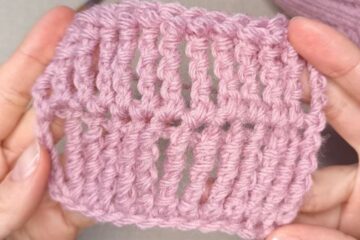 Hands holding a small swatch of pink knitted fabric, showcasing a detailed triple treble crochet stitch pattern.