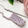 A small piece of purple crochet work with a crochet hook and strands of yarn on a white surface.