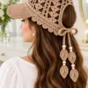 Warm tan crocheted ponytail cap with lace mesh crown, curved visor, and leaf applique ties with pearl beads, shown from the back on brunette hair