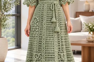 Sage green crocheted mesh dress with V-neckline, daisy appliqués along vertical bands, elbow sleeves, and tie waist worn by woman in bright room