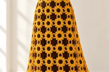 Golden yellow crocheted sunflower maxi dress with chocolate brown centers displayed on a white dress form in soft natural light